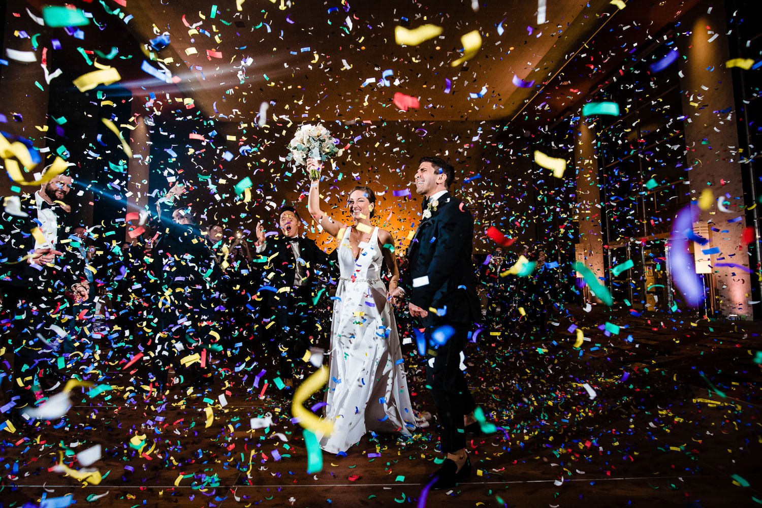 A newly married couple cheering in the midst of confetti