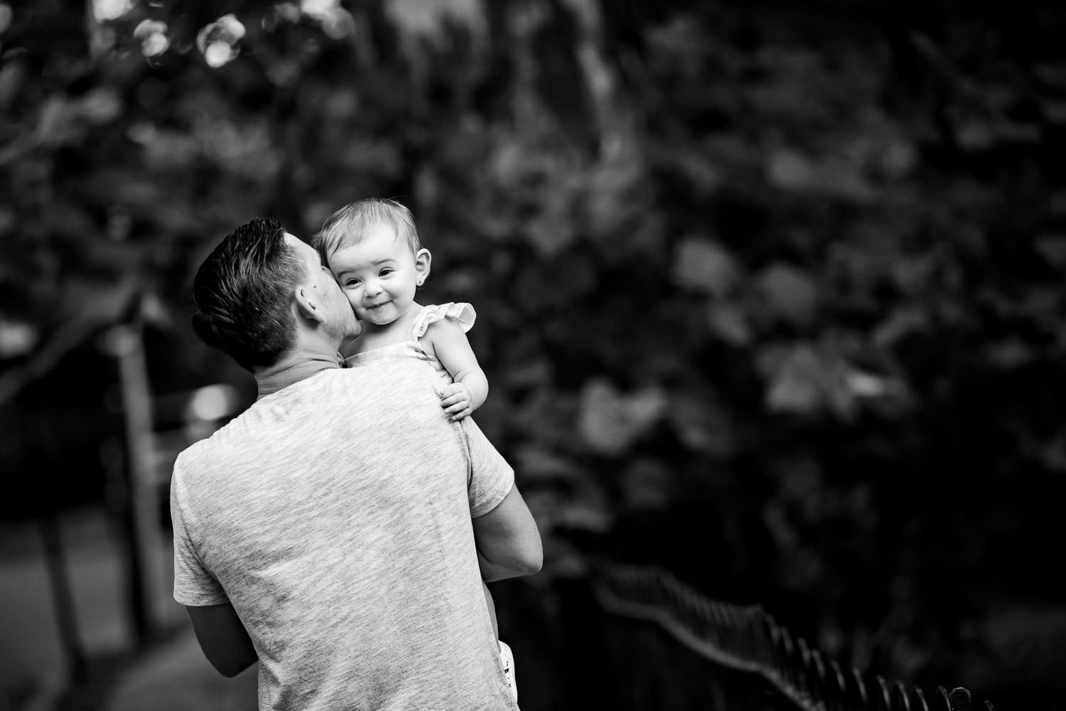 A baby girl smiling as her dad kisses her cheek