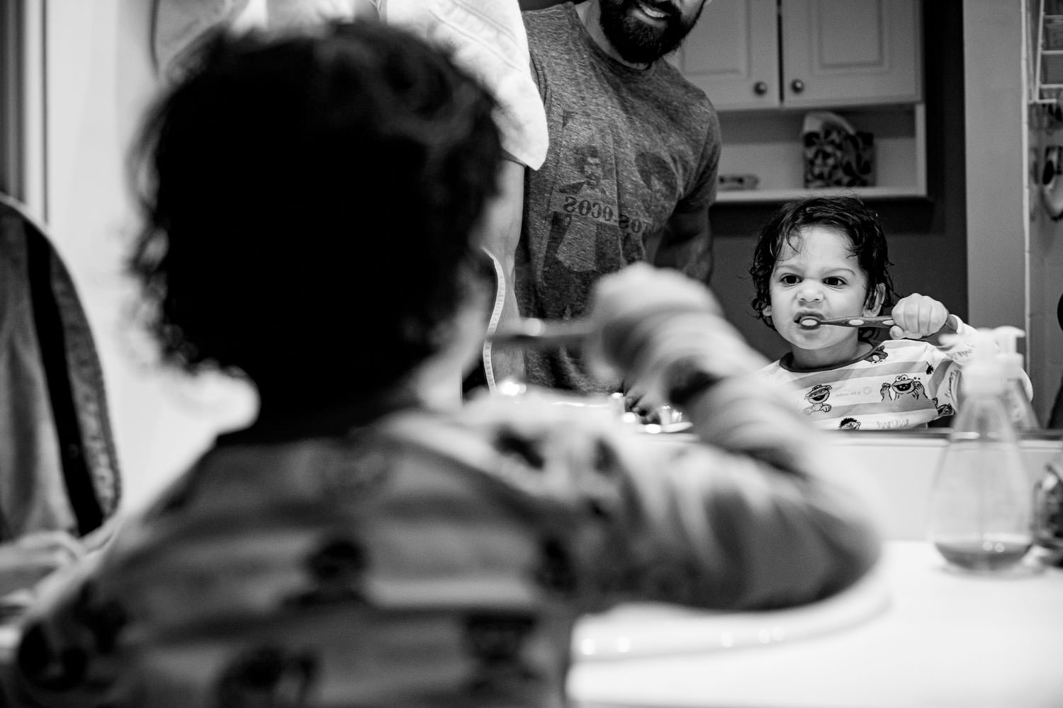 A kid brushing his teeth while his father looks on